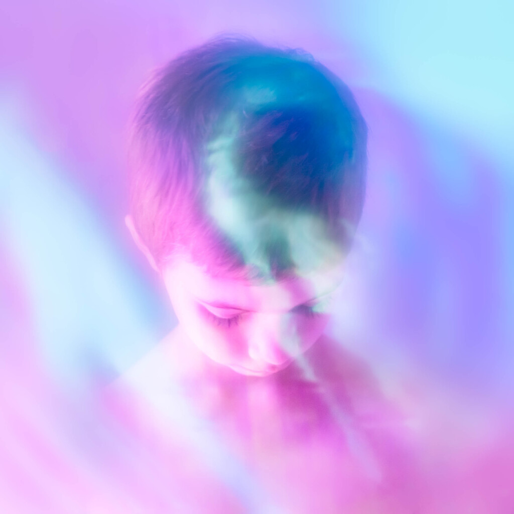 A child looking down. Just the head and shoulders are visible. The photo is pink and purple and there is a glare in the middle. 