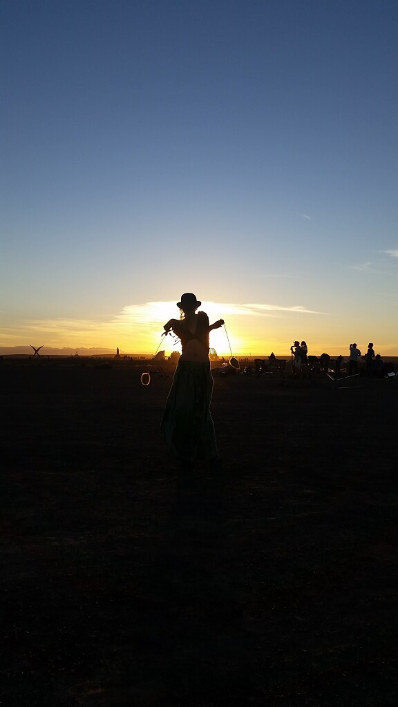 Silhouette of someone playing with poi backlit by the sunset