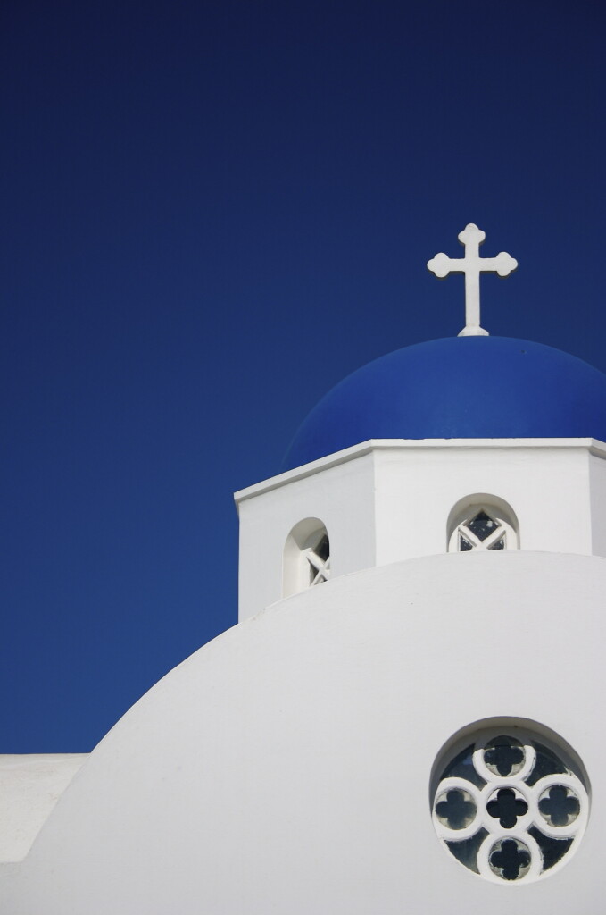 Photograph of a blue church domed roof on Santorini. The blue of the roof is very similar to the deep blur of the sky behind. The rest of the building is bright white.