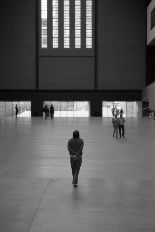 Photograph from behind of a person in the middle of the Turbine Hall at the Tate Modern in London. They are looking up.