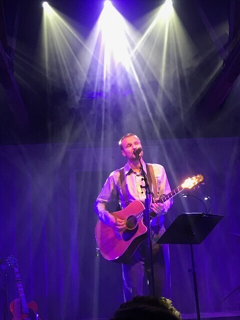 A music performer on a dark stage with visible light rays behind him