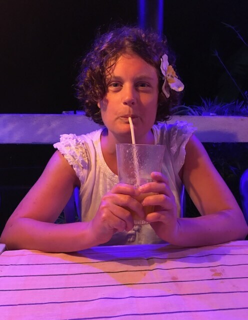 A woman at a beach restaurant in Thailand, enjoying a drink and looking pretty pleased