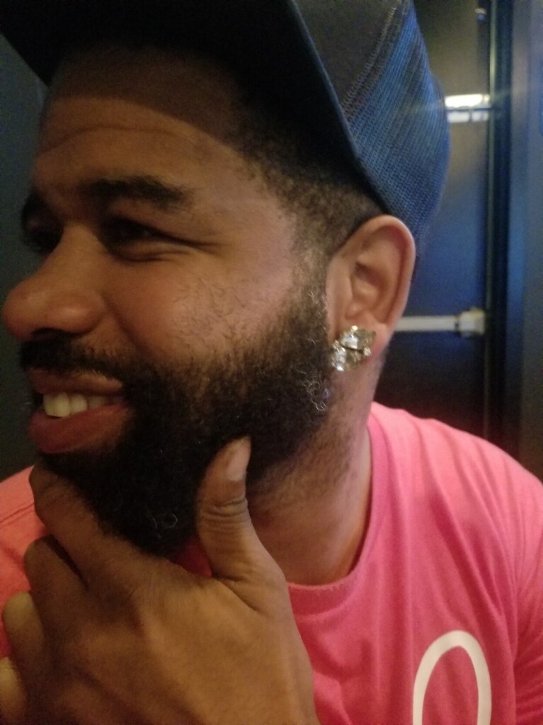 This is one of my best friends 🥰 He's a Black man with a short but full beard. He's turned in profile, with his hand on his chin. He's wearing a black baseball cap and a vintage silver and white clip on earring that is mine lol
