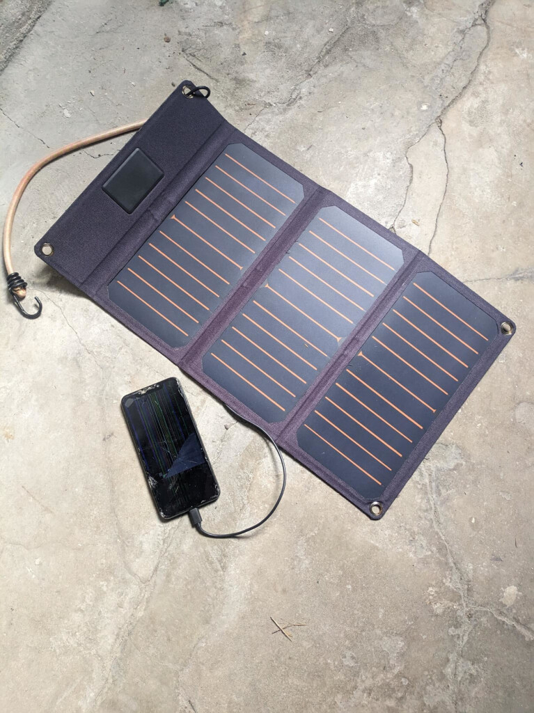 a cellphone with a broken screen is lying on a dirty concrete floor next to a solar charger