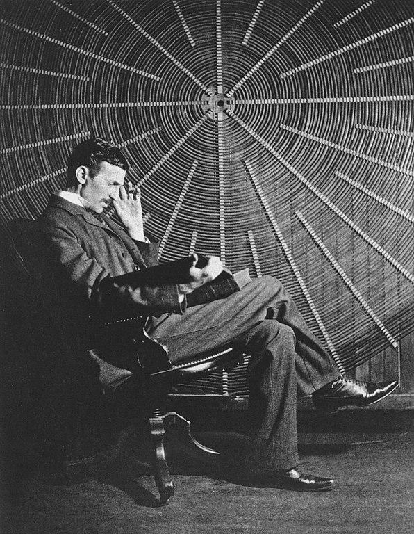 Nikola Tesla, with Rudjer Boscovich's book "Theoria Philosophiae Naturalis", in front of the spiral coil of his high-voltage Tesla coil transformer at his East Houston St., New York, laboratory.

Tesla is typically shown standing confidently, either holding the book or with it placed on a nearby table, symbolizing the connection between theoretical knowledge and practical application. He is dressed formally, reflecting his professional demeanor and the serious nature of his work.