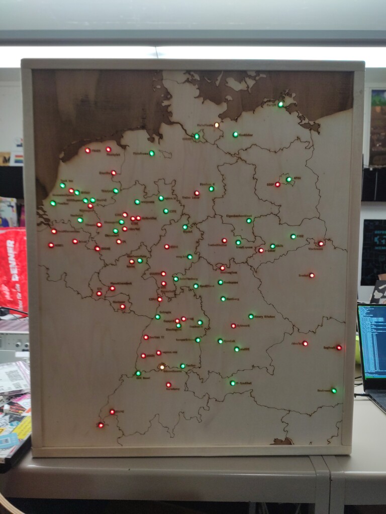 A map of a part of Europe (predominantely DE, CH, AT, CZ, NL, BE, LU) laser-engraved into plywood, mounted in a wooden frame. There is a total of 83 LEDs in the map, each labeled with the name of a hackerspace in that location. The LEDs glow either green or red, depending on whether the corresponding hackerspace is currently open or closed.