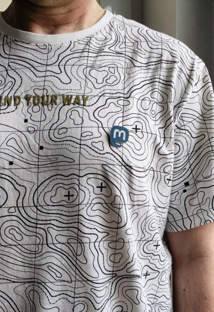 Przypinka z logo mastodon przypięta do koszulki w poziomice. 