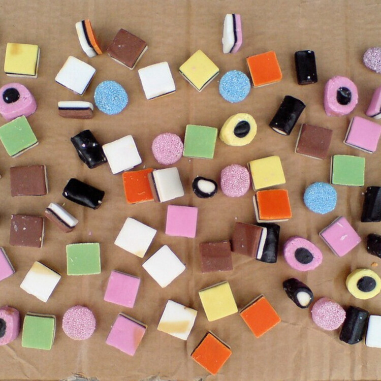 A selection of sweets from a licorice allsorts assortment, spread out on a piece of brown cardboard.