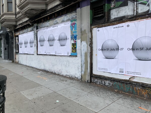 A wall covered in giant ads from Worldcoin. These are wheatpasted up, probably without permission. Each one is about 4 feet tall and shows the silver orb that Worldcoin uses for scanning retinas. 