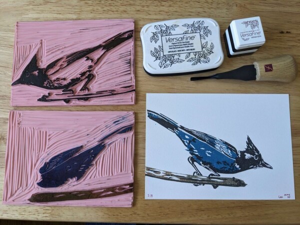 A hand-carved blue jay stamp with supplies on a table.