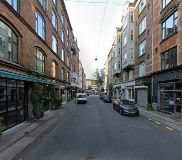 Google streetview photo of Vaernedamsvej in Frederiksberg. 3/4 of the space is dedicated to cars, not to humans. Parked cars visible on both sides of the street.