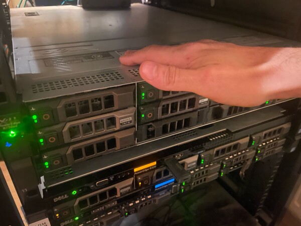 Ręka położona na serwerze u samej góry szafy z serwerami. 

