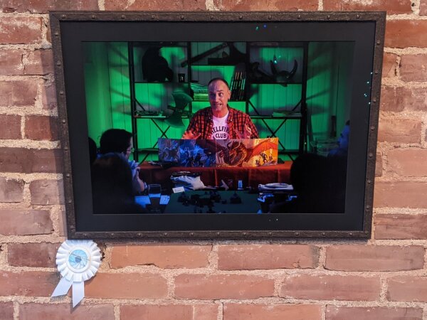 Photo of a framed picture on a brick wall, with an honorable Mention ribbon attached.