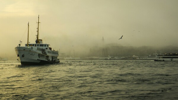 Eine alte Fähre auf dem Bosporus im Nebel und Gegenlicht. Möwen über dem Wasser. Gebäude im Hintergrund / am Ufer unscharf.