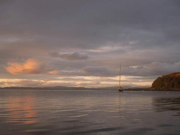 Single yaght moored on mirror calm see with orange sunset reflected on clouds