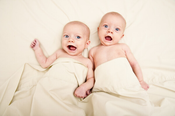 Two infants in beige sheets looking at the camera and smiling. 
