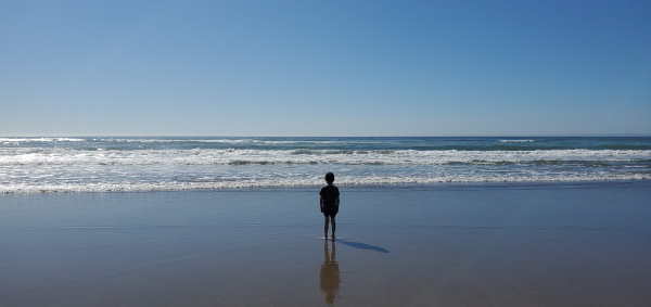 A child on the beach, small and silhouetted against the ocean and a blue sky