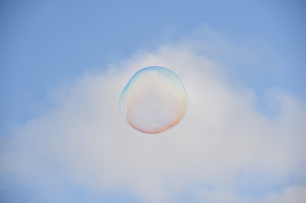 A large soap bubble, the blue sky and a large, gray fluffy cloud behind it.