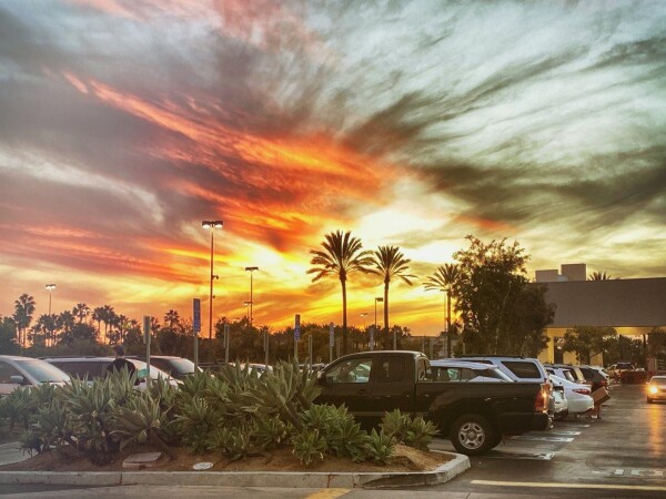 A parking lot with a swirl of clouds in the sky stretching out into dusk as the sun lowers itself into the horizon and shows off it's beautiful orange and yellow colors.
