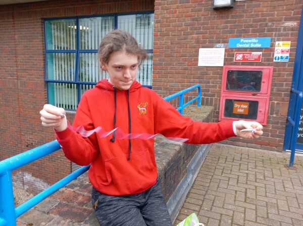 A teenager in a red top has a look of deep concentration. His hands are held wide apart, and between them is a blur of a thin, pale, wiggly line.