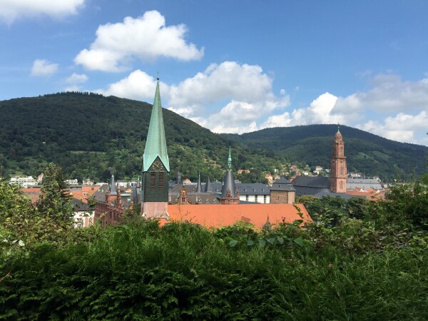 View of Heidelberg from a hill with the pretty green copper tower of Peter’s church and the red sandstone tower of Jesuit church in front of rolling hills.