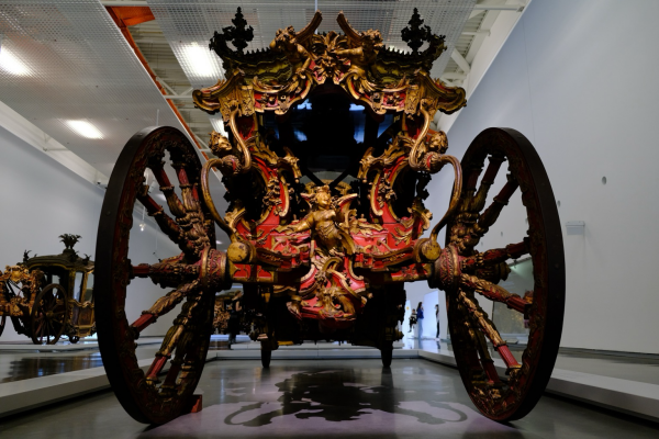 Low-angle photo of a royal carriage from the rear. Everything from the spokes of the wheels to the roof is covered in red-and-gold carved wooden sculptures