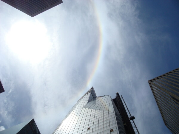 Picture looking up at blue sky with faint rainbow between skyscrapers