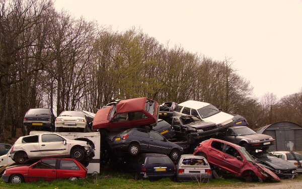 A French auto wrecking yard: a pile of damaged cars in a field, bordered by trees.