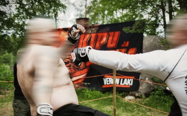 a photo posted on Veren Laki’s Telegram channel of the combat sports fights, showing a large rock in the background, as well as a chimney (Bellingcat has cropped the photo from the original to obscure neo-Nazi symbolism). 