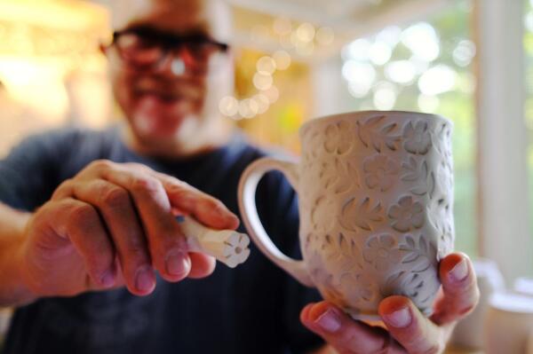 Me holding a handmade clay stamp and wheel thrown cup with stamped textures. It’s a pretty cup