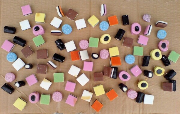 A selection of sweets from a licorice allsorts assortment, spread out on a piece of brown cardboard.